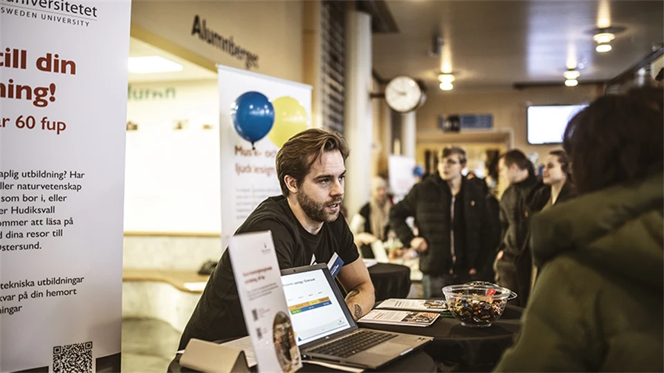 En manlig student står bakom ett bord och ger information till elever på Öppet hus. 