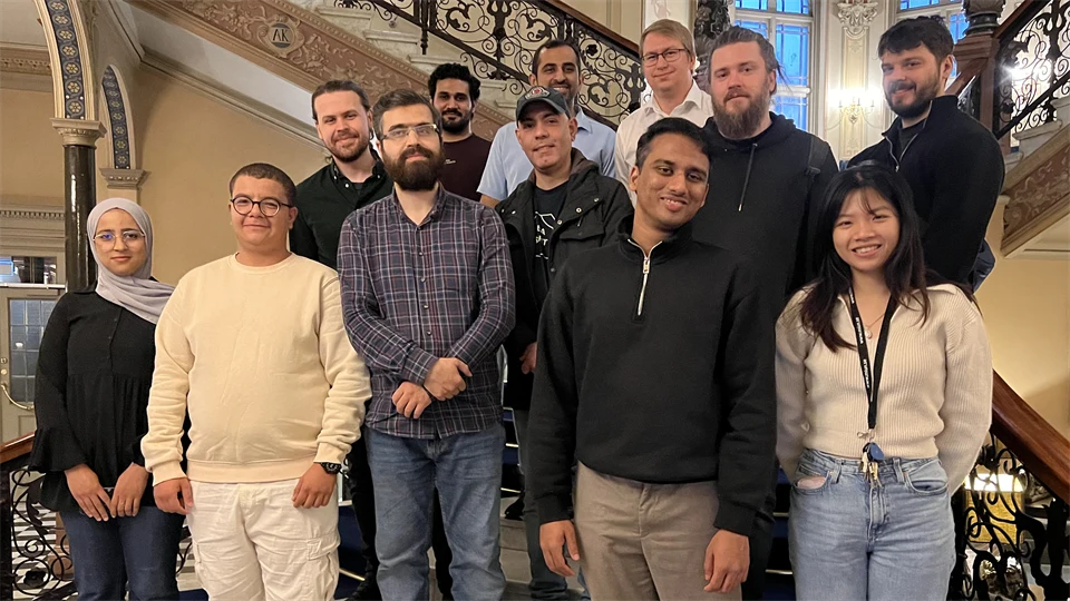 A group of people are standing together on a staircase, looking into the camera and smiling.