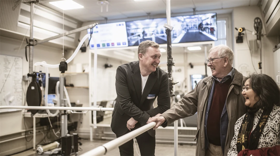 Man står lutandes mot staket och ler mot glad kvinna och glad man i ett forskningslabb. 