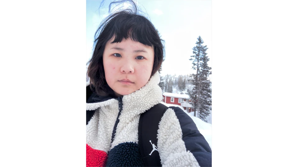 A young woman with black hair is walking in a snowy winter landscape wearing a shaggy fleece jacket in white, red and dark blue.