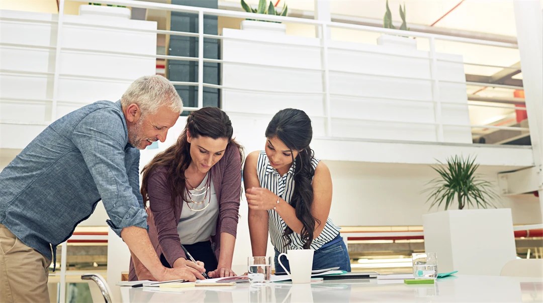 Tre personer står vid ett skrivbord och kollar på ett dokument