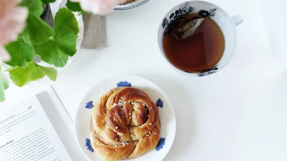 En kopp te och bulle på ett vitt bord med blomma i förgrunden