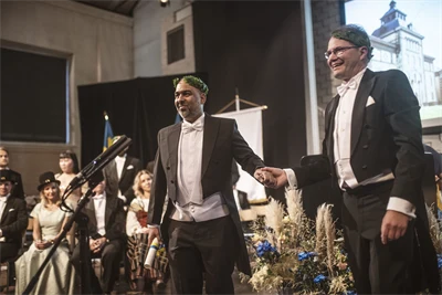 Två finklädda personer med lagerkransar står på en scen.