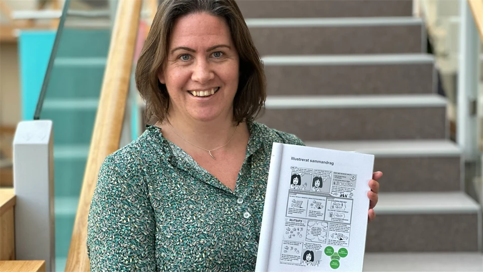 En brunhårig kvinna håller upp sin avhandling framför en trappa