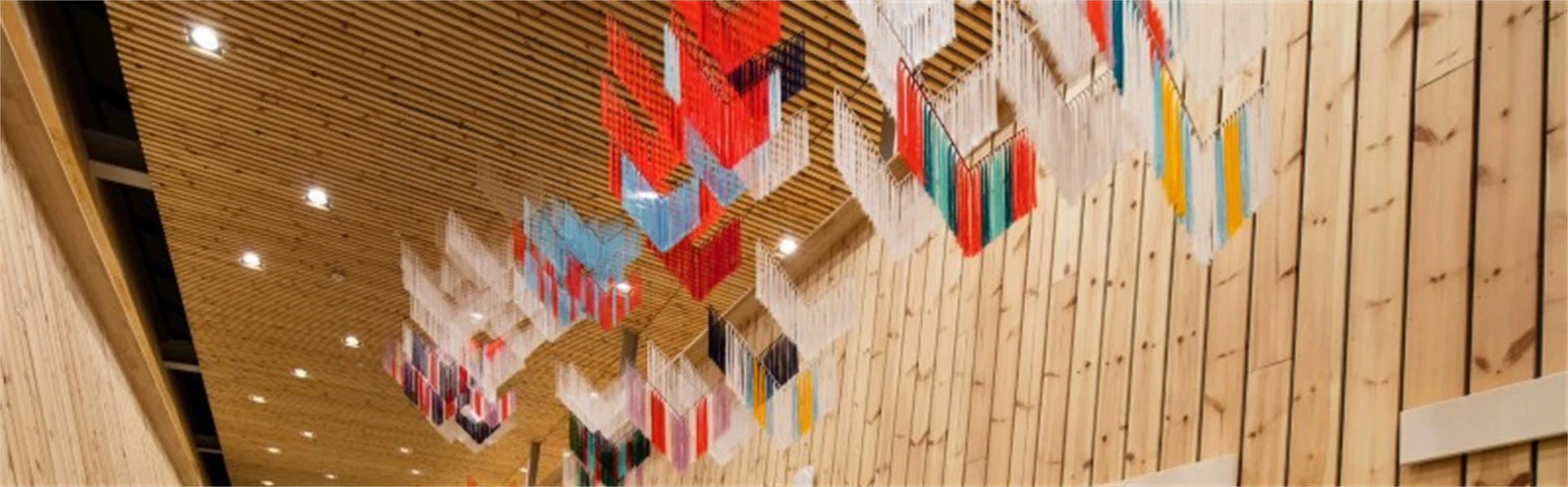 Konstverk av trådar i formen av samiska sidensjalar hänger från taket i träbyggnad av modern arkitektur.