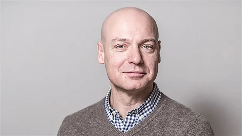 Ett porträttfoto av en man med rakat huvud och grå tröja