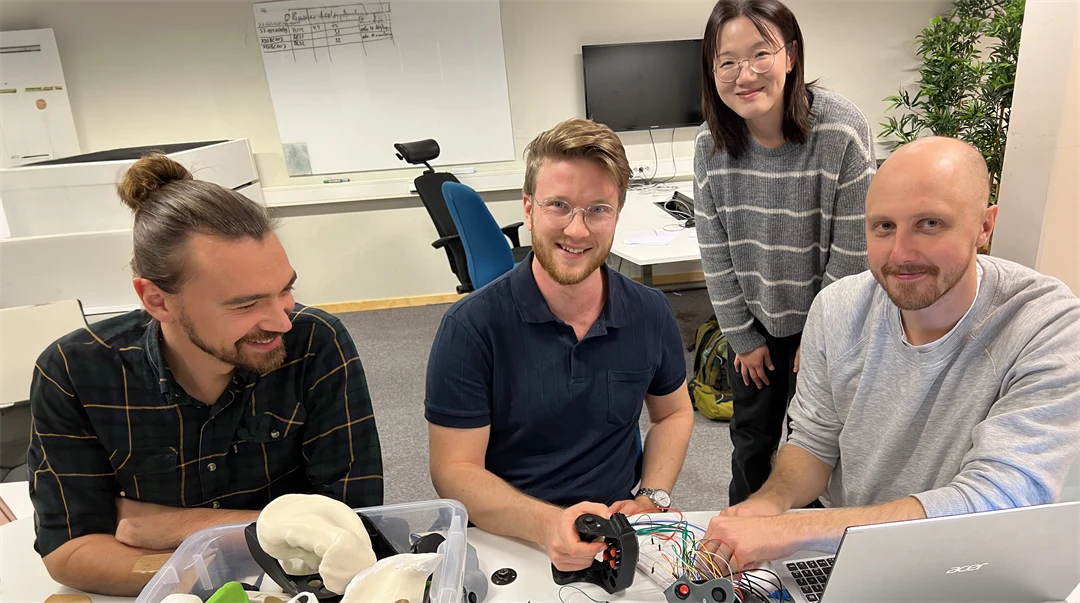 Några personer är tillsammans vid ett bord med elektronik och andra saker i en plastlåda.