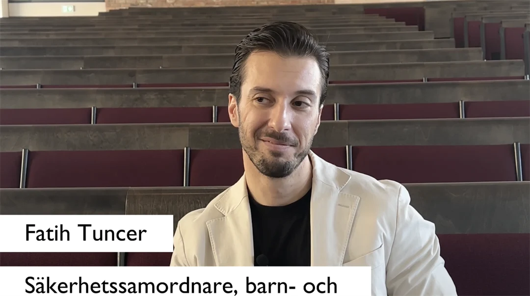 Man sitter med benen korsade och lutar sig bakåt under en intervju i en tom föreläsningssal.