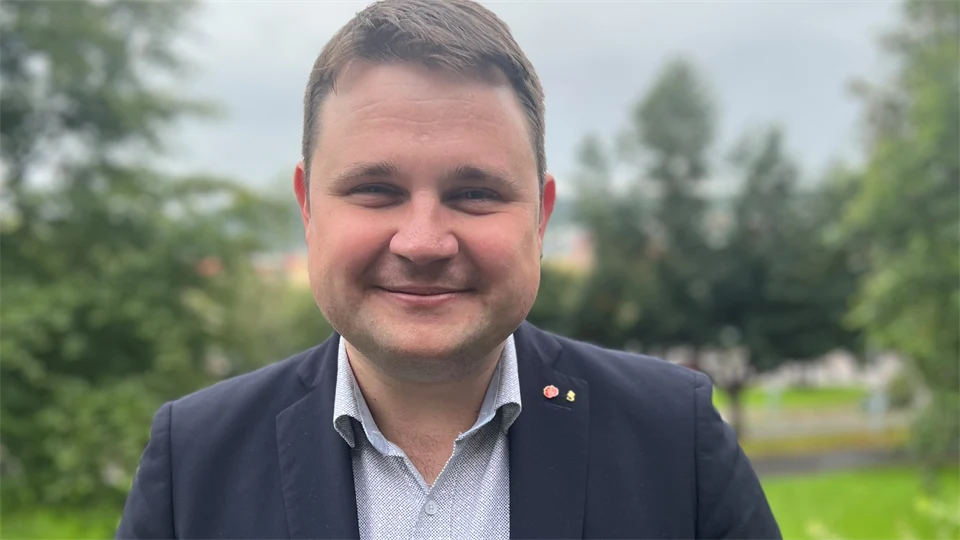 Porträttbild av leende mörkhårig man i mörk kavaj och grå skjorta