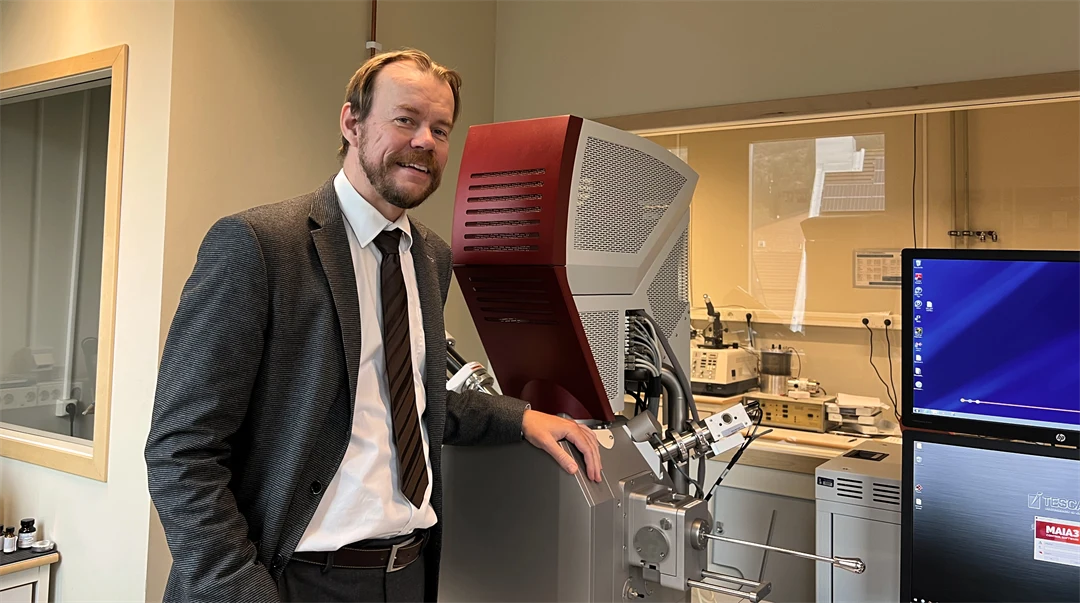 En man står framför laboratorieutrustning och bildskärmar.