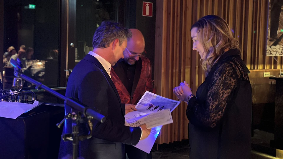 Pristagare med presentkort och pris i handen pratar med en man och en kvinna. 