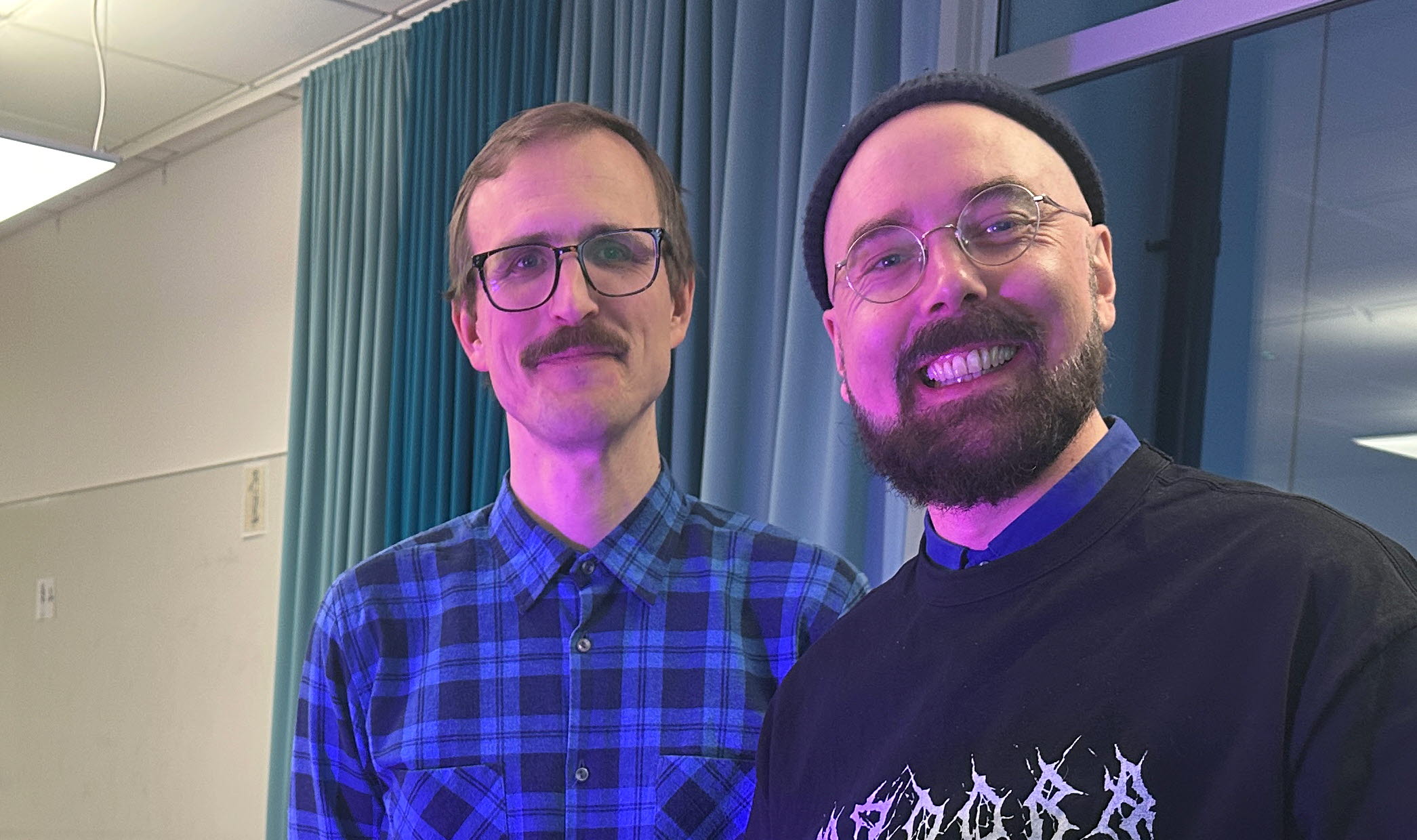 Två leende män framför en vägg