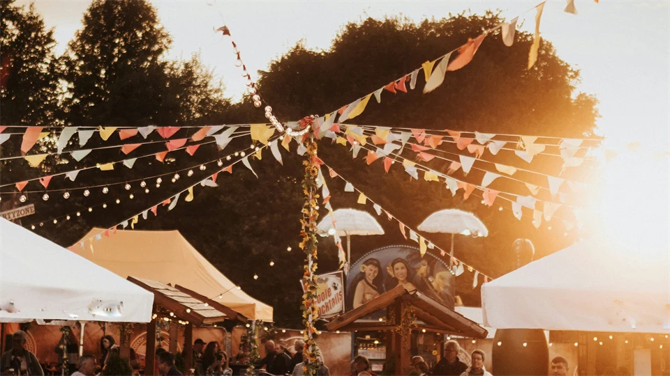 Festival med besökare, tält och vimplar i kvällsljus.