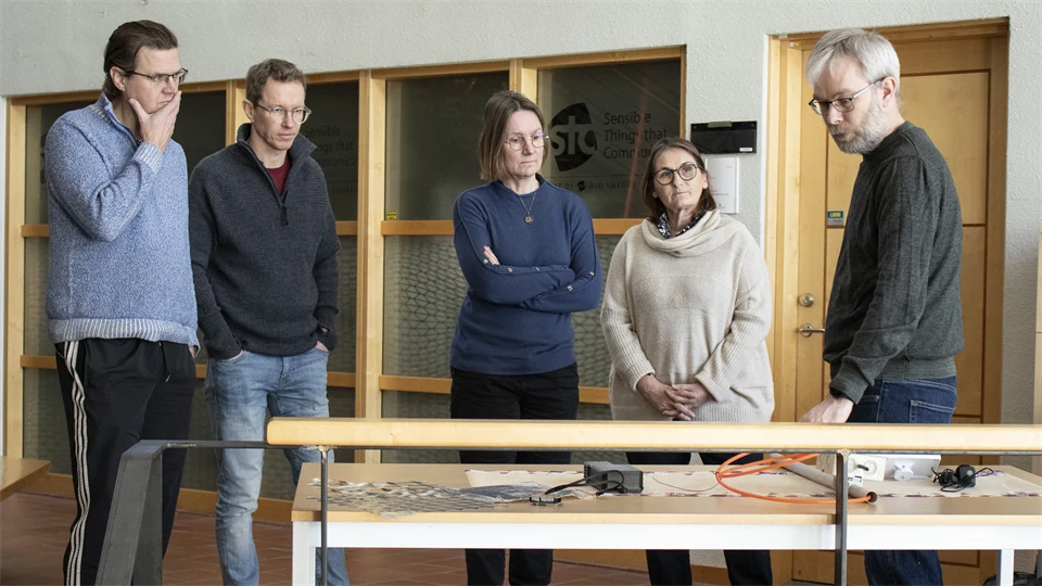 Four people stand and listen to a man who talks about various prototypes produced in research projects.
