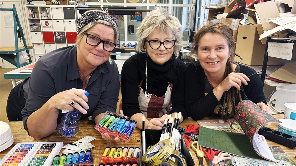 Tre kvinnor framför ett bord med konstnärsmaterial