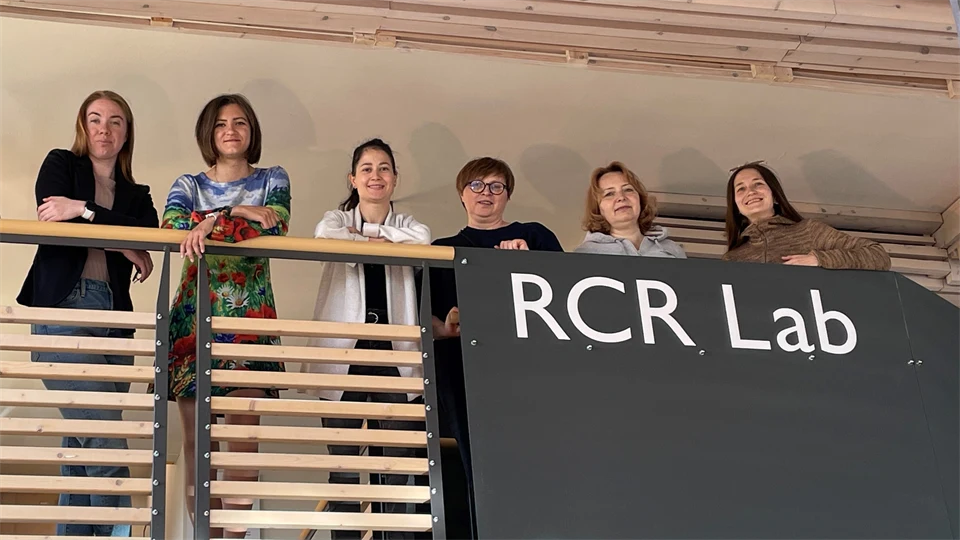 Sex kvinnor står vid ett räcke och tittar neråt. På räcket står texten RCR Lab med stora bokstäver.