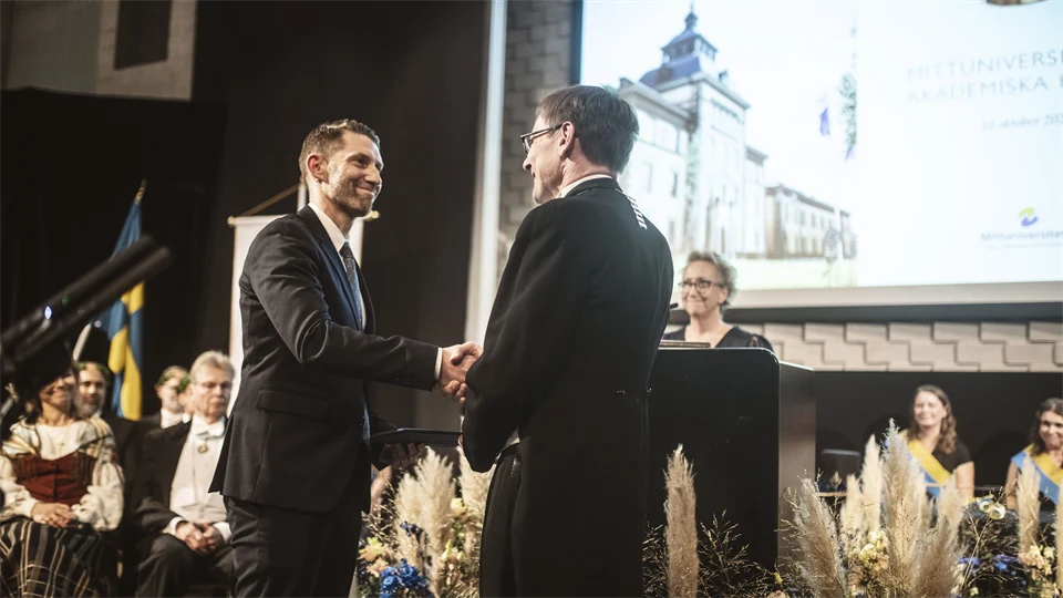 Två finklädda män skakar han på en scen. 