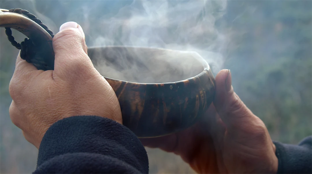 Två händer som håller en guksie, kåsa, med rykande kaffe. 