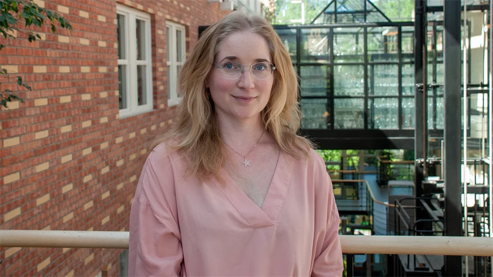 Woman with fair, long hair, glasses and a pink blouse poses in front of the camera.