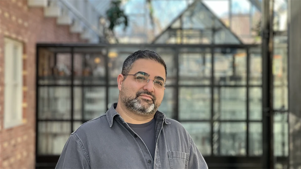 A man stands in a courtyard, he looks into the camera.