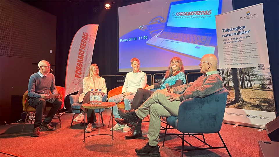 Five people sit on chairs on a stage in front of a screen.