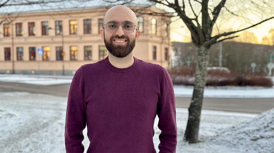 Leende man med rakat huvud, brunt skägg och glasögon. Han har vinröd tröja och står utomhus. Årstiden är vinter.