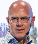En man i rutig skjorta och glasögon med ett grönt nyckelband runt halsen.
