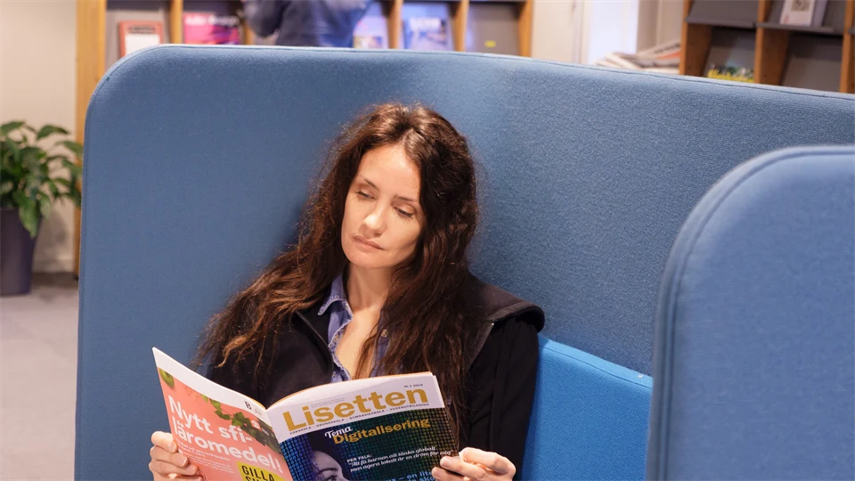 Kvinna läser tidning sittandes i en blå soffa på ett bibliotek