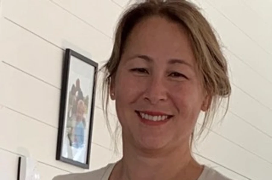 Bild på en kvinna som arbetar på folkhälsomyndigheten. Hon har uppsatt hår och ler. Bakgrunden är en vit trävägg med liggande bräder