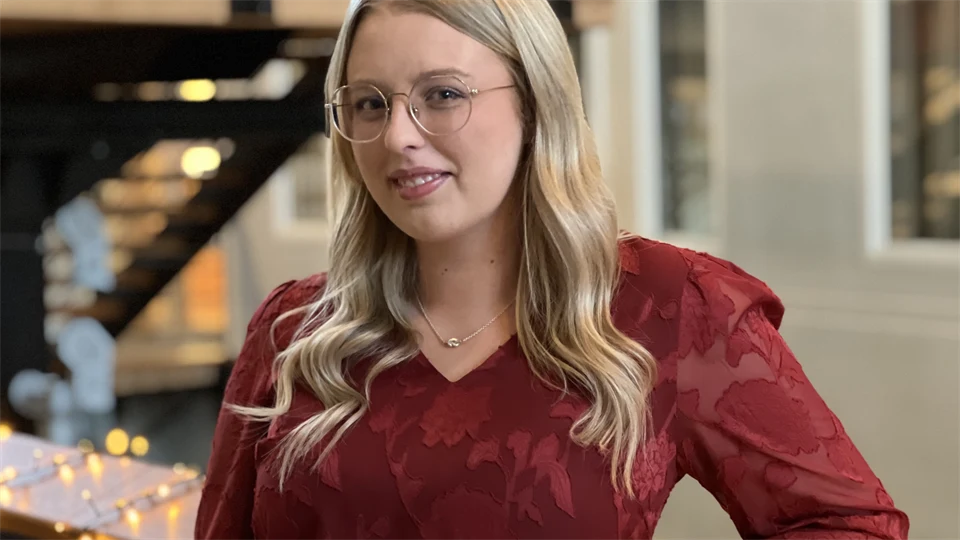  A young woman with long hair and glasses looks into the camera.