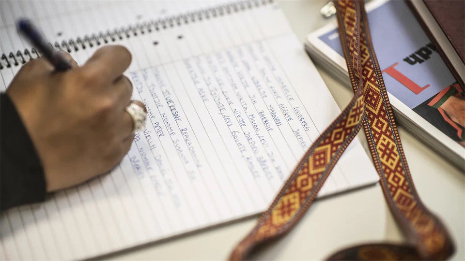 Hand som skriver i ett block intill ett samiskt band