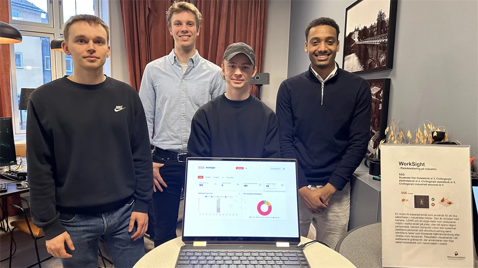 Fyra unga män står bakom en laptop