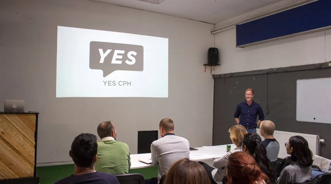 Grupp sitter vid bor i ett rum och tittar på en presentation