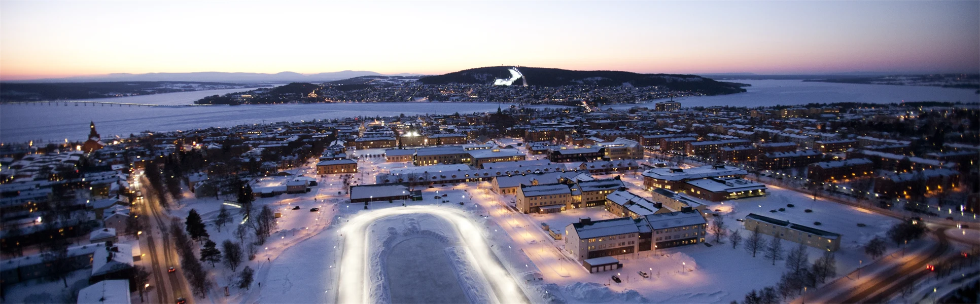 Fågelvy över en stadsbild med en sjö och fjäll i bakgrunden