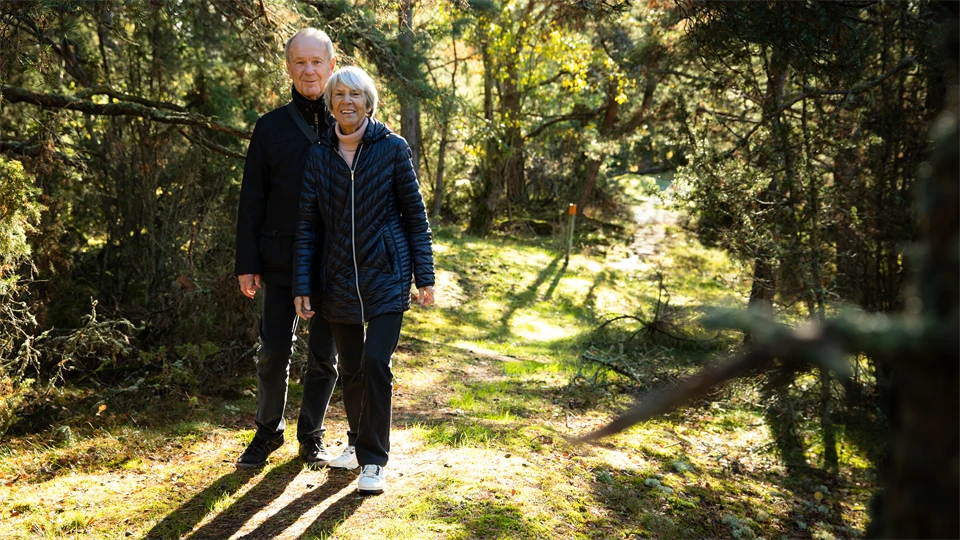 äldre par på skogspromenad, det är grönt och solen skiner