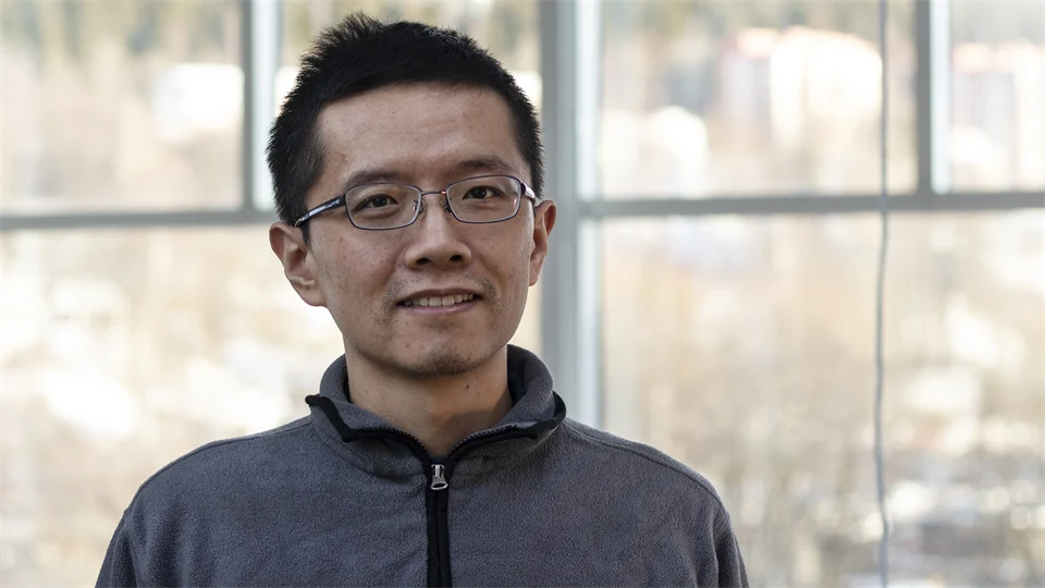 An Asian man with glasses, dark hair and a gray sweater.
