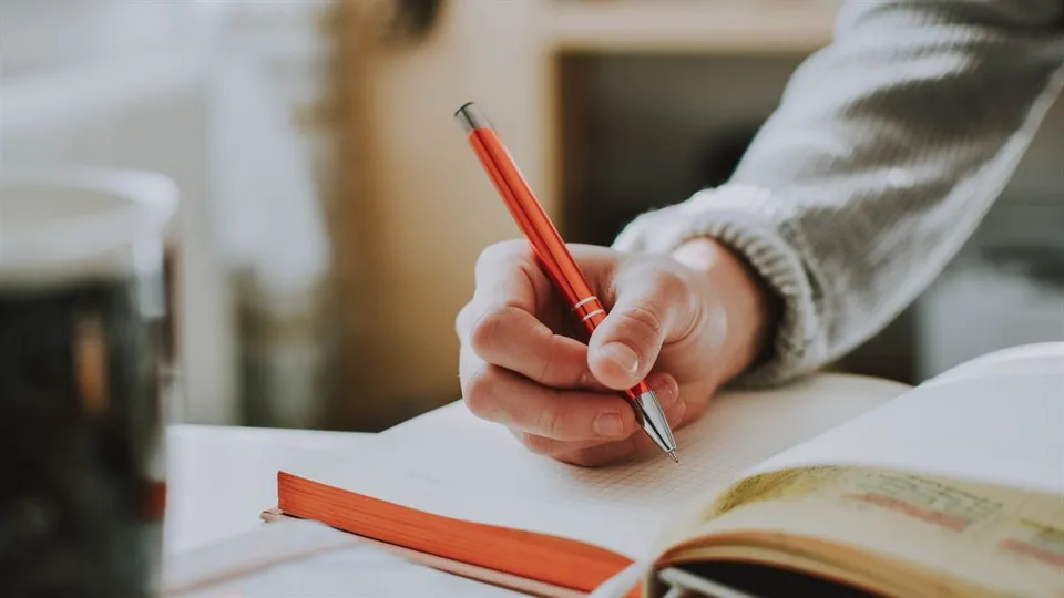  A hand holding a pen and taking notes in a notebook