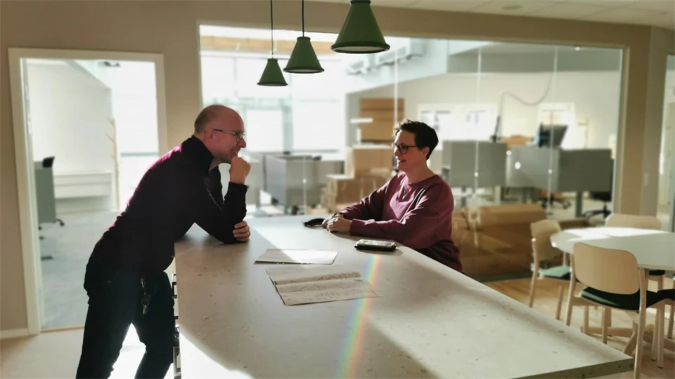 Två personer samtalar vid en köksö i ett ljust kontorsutrymme.