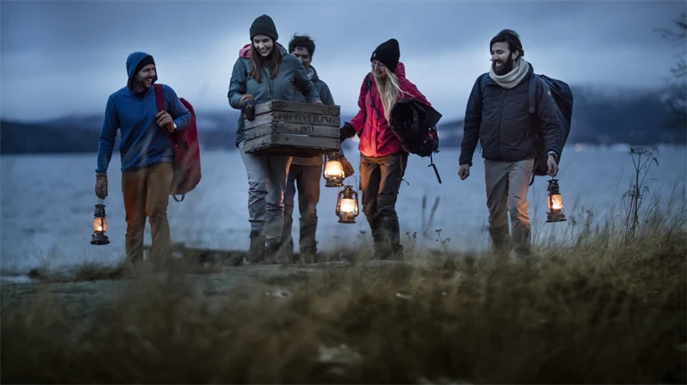 Five people walk with lanterns by the beach at he High Coast in Sweden