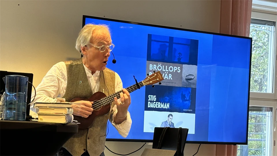 en man spelar ukulele framför en blå skärm