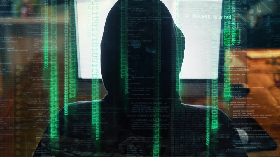 En person i hoodie sitter framför en datorskärm med texten "Access Granted", omgiven av grön kod som antyder ett intrång eller cyberattack.