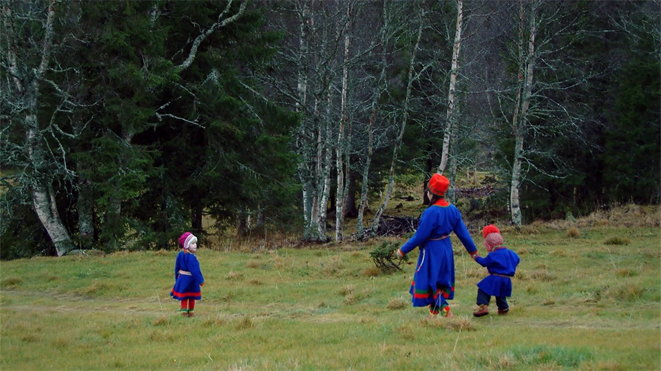 Kvinna och två barn i sydsamiska dräkter går över ett fält.