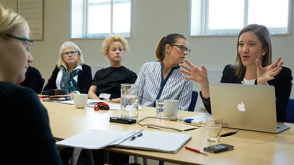 Fem kvinnor sitter vid ett konferensbord och diskuterar.