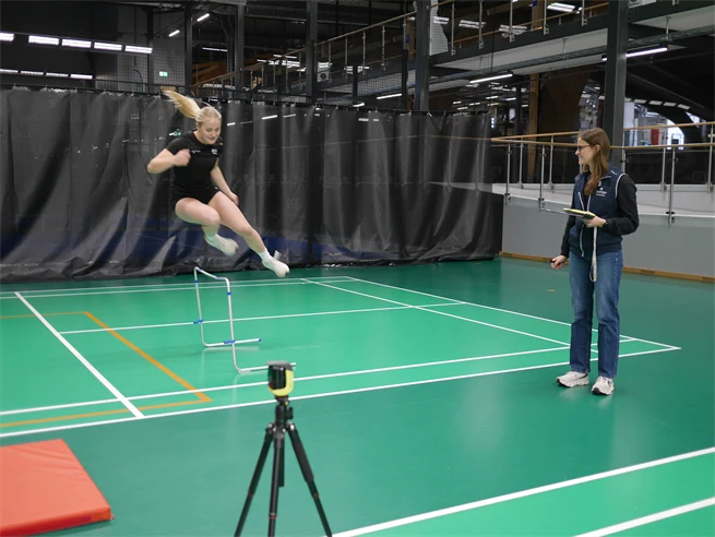 En ung kvinna hoppar över ett hinder i en sporthall.