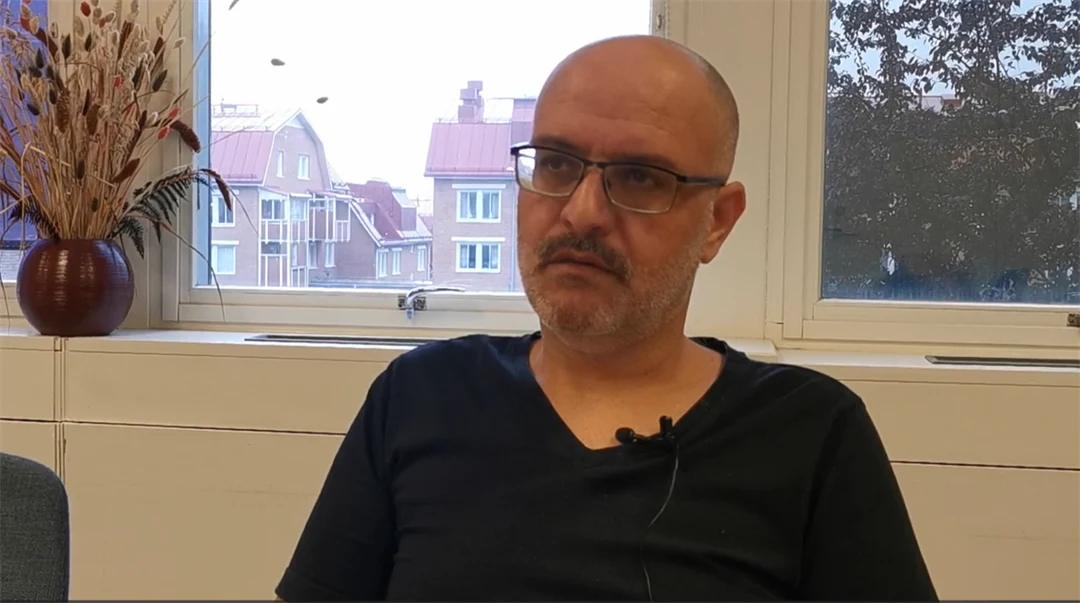 A man wearing glasses and a black shirt is being interviewed
