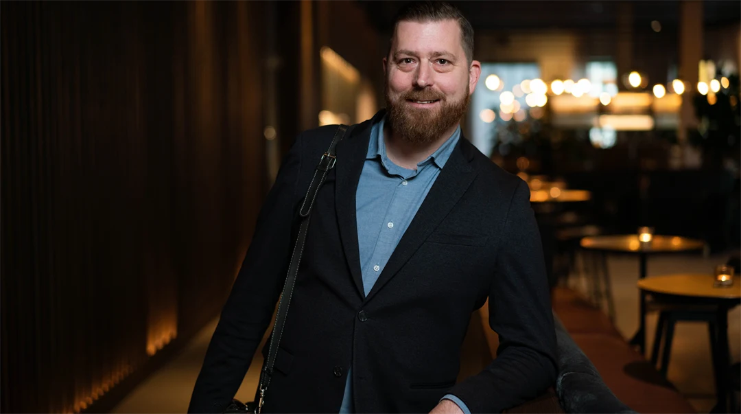 En man står i ett mörkt rum med några mindre bord i bakgrunden.