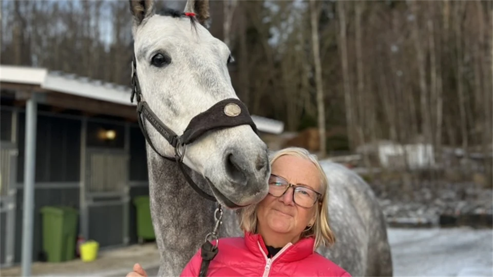 En kvinna står utomhus med en häst vid sin sida.