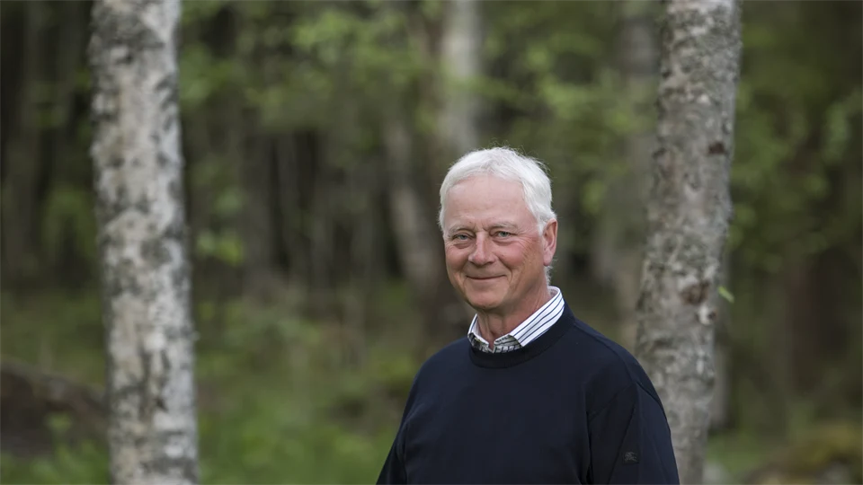En man i mörk tröja står i en skog.