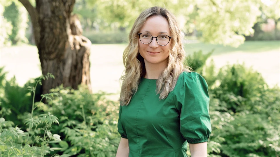 Kvinna med mellanlångt ljust hår och glasögon. Hon bär en grön festklänning.