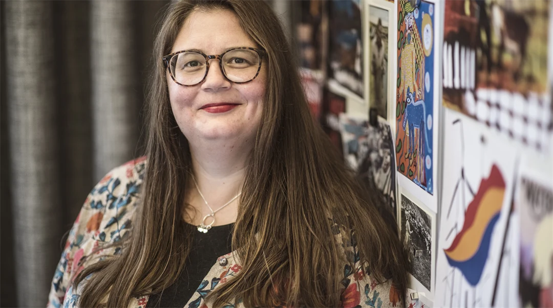 A woman is standing next to a beige curtain.